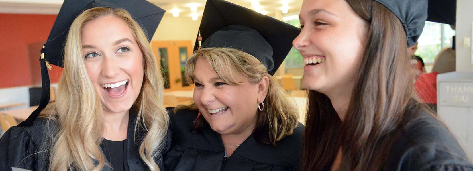 Three Grads in caps and gowns hugging