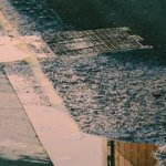 Water flowing into a storm drain by a sidewalk.