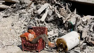 A young Palestinian sits in an armchair among the ruins of Gaza City.