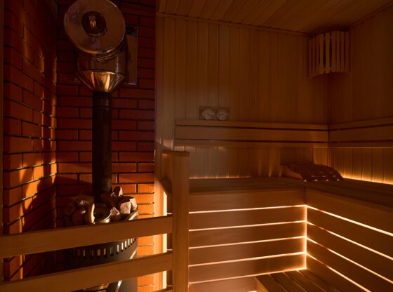 Russian sauna bathhouse with muted intimate light from under the bottom of bench wooden lantern hygrometer thermometer with sauna stove oven with internal stone heater and stones and chimney or pipe.