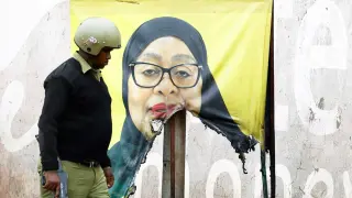 A Tanzanian riot police officer walks past a vandalized campaign sign for President Samia Suluhu.