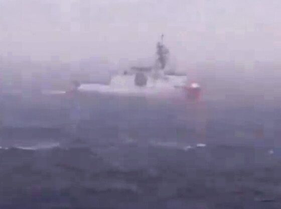 A white and red warship on dark blue, choppy water.
